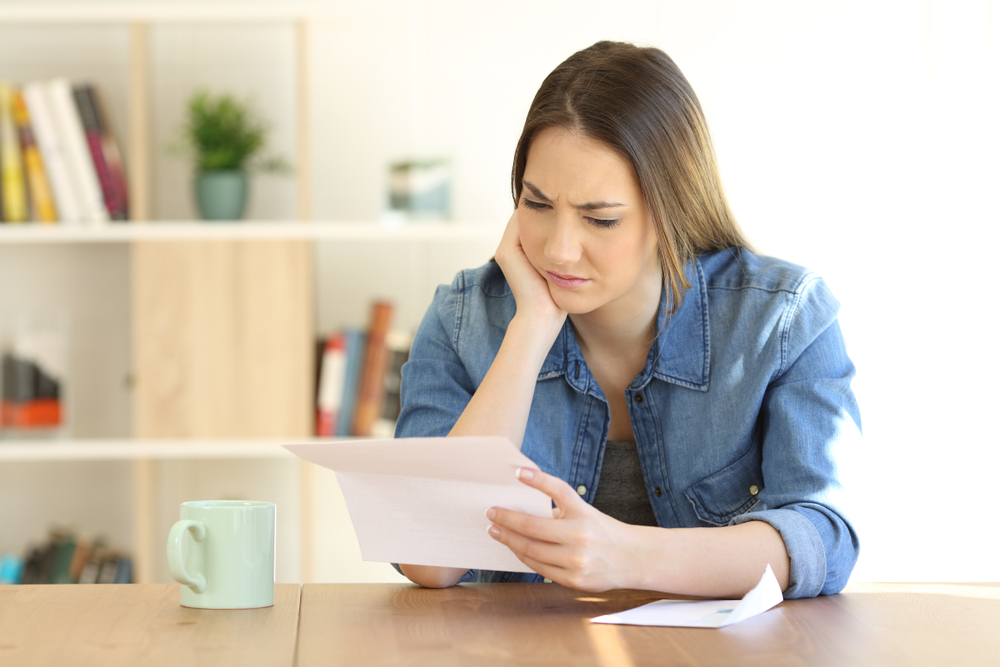 portrait of a worried female reading a paper letter on a table at home