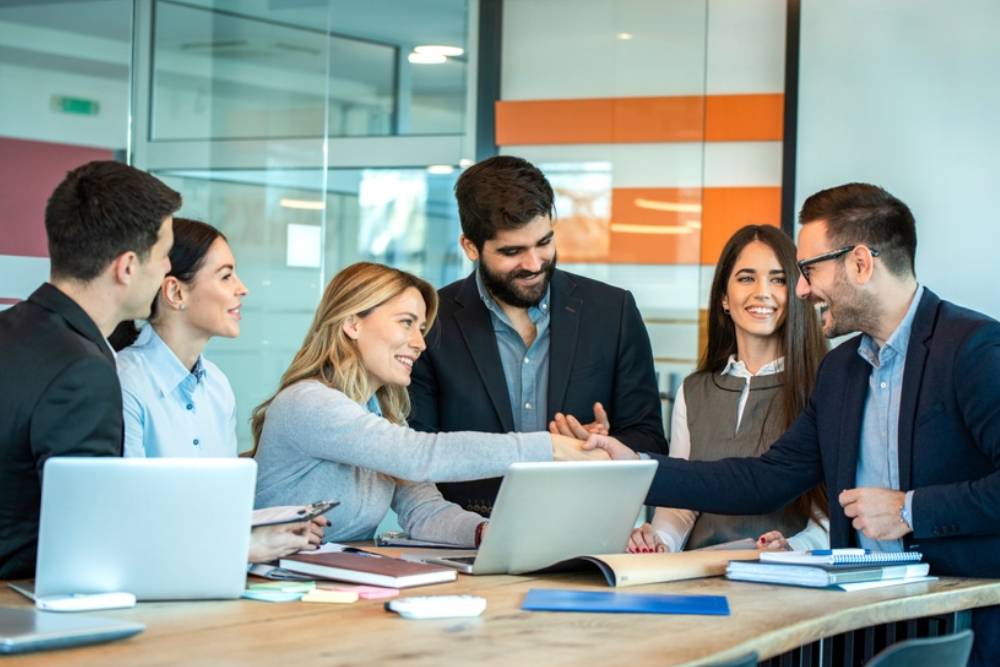 Professional business team celebrating successful project completion with handshake and smiles